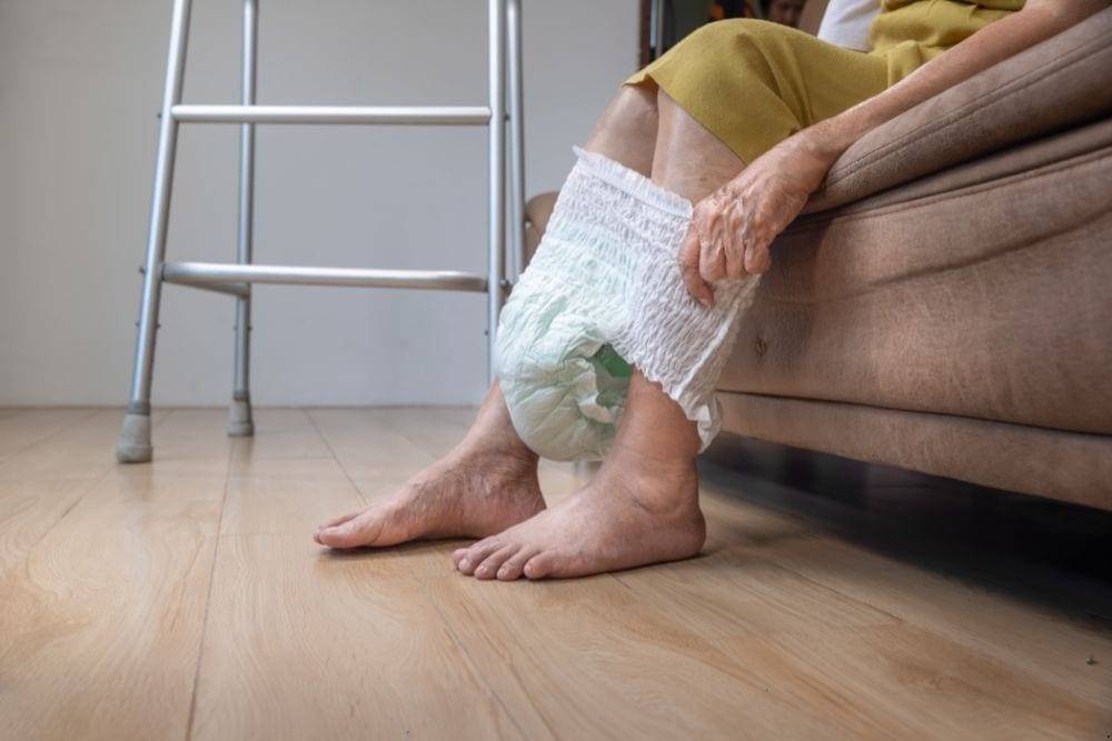 a carer is helping an elderly patient with incontinence wear a diaper