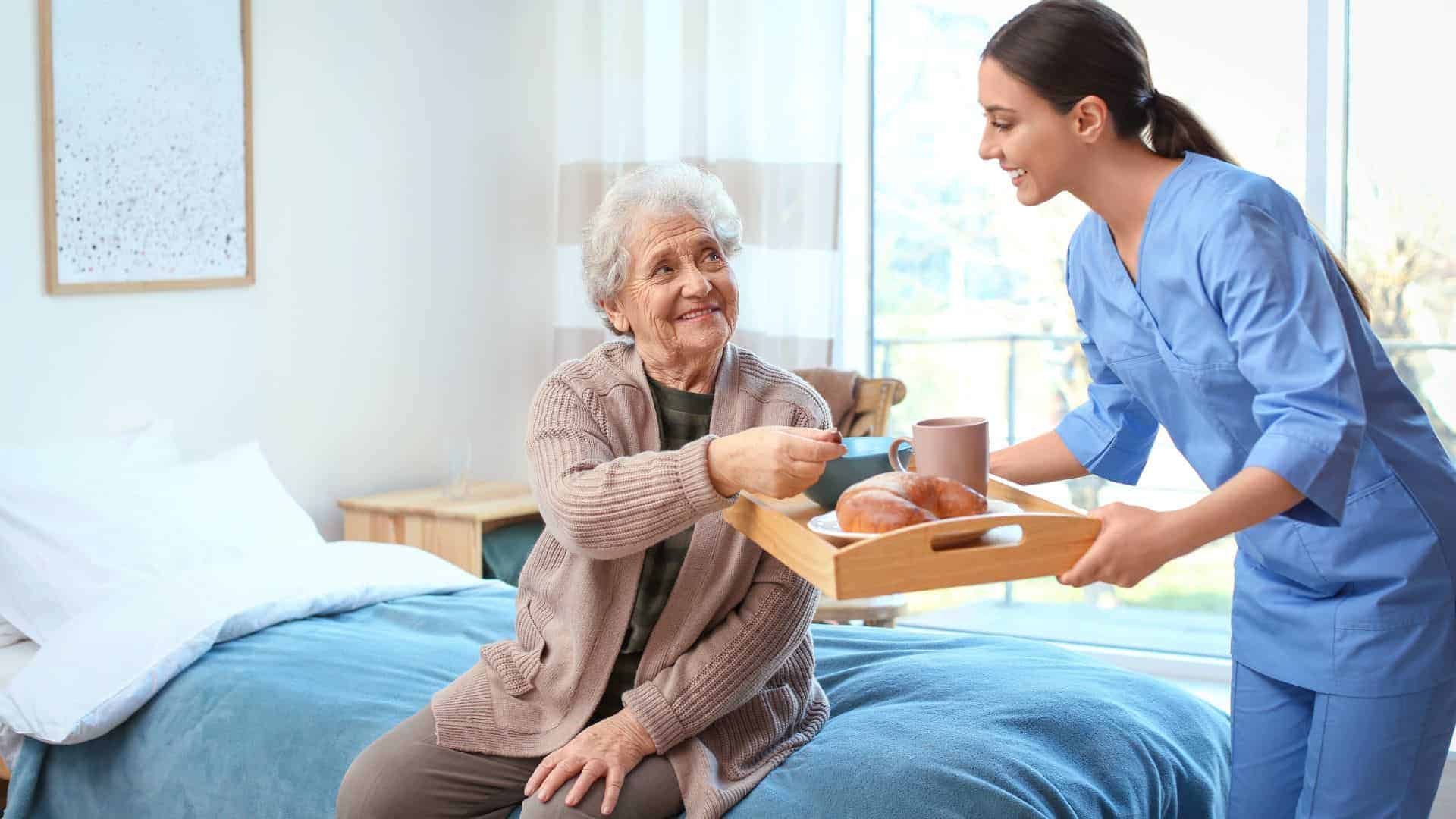 in-home caregiver serving lunch to a senior woman