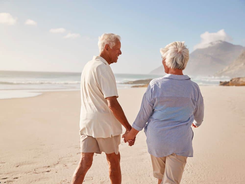 A senior couple walking on the beach while happily holding hands.