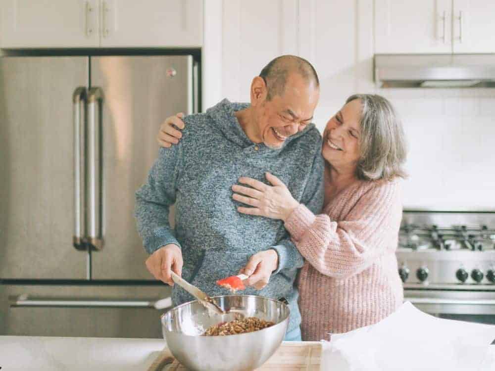 A senior couple happily cooking in the kitchen.