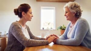 daughter holds her senior mother's hand, offering family support while discussing the early signs of dementia in their Reno home.