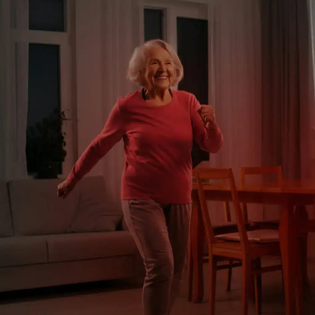A friendly, healthy-looking senior woman (70s) with a bright smile, marching in place in her living room.
