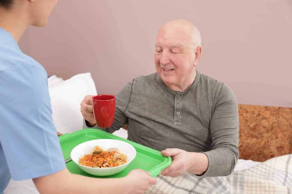 A caregiver providing meal assistance to a resident, a service that factors into senior care costs.