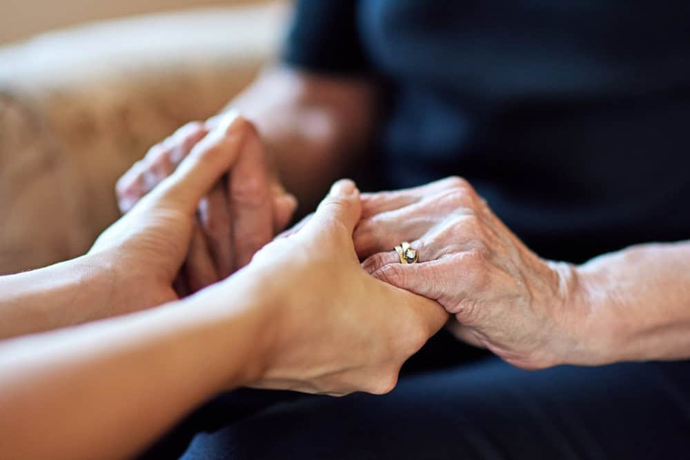 A close-up of a caregiver holding a senior's hand in a warm living room.
