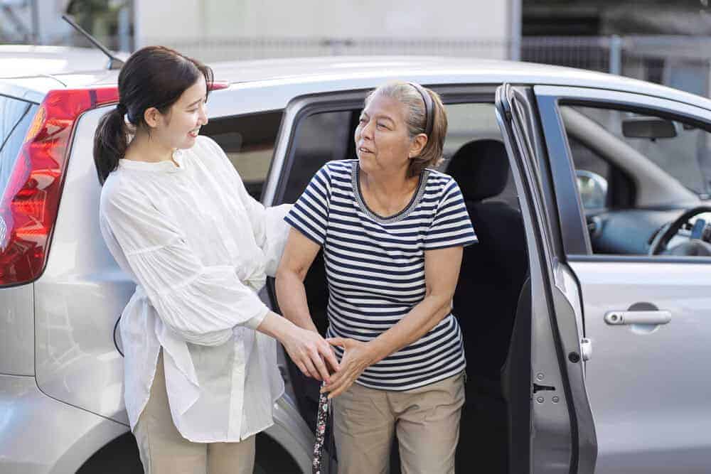 Caregiver assisting a senior woman out of a car in Carson City, NV.