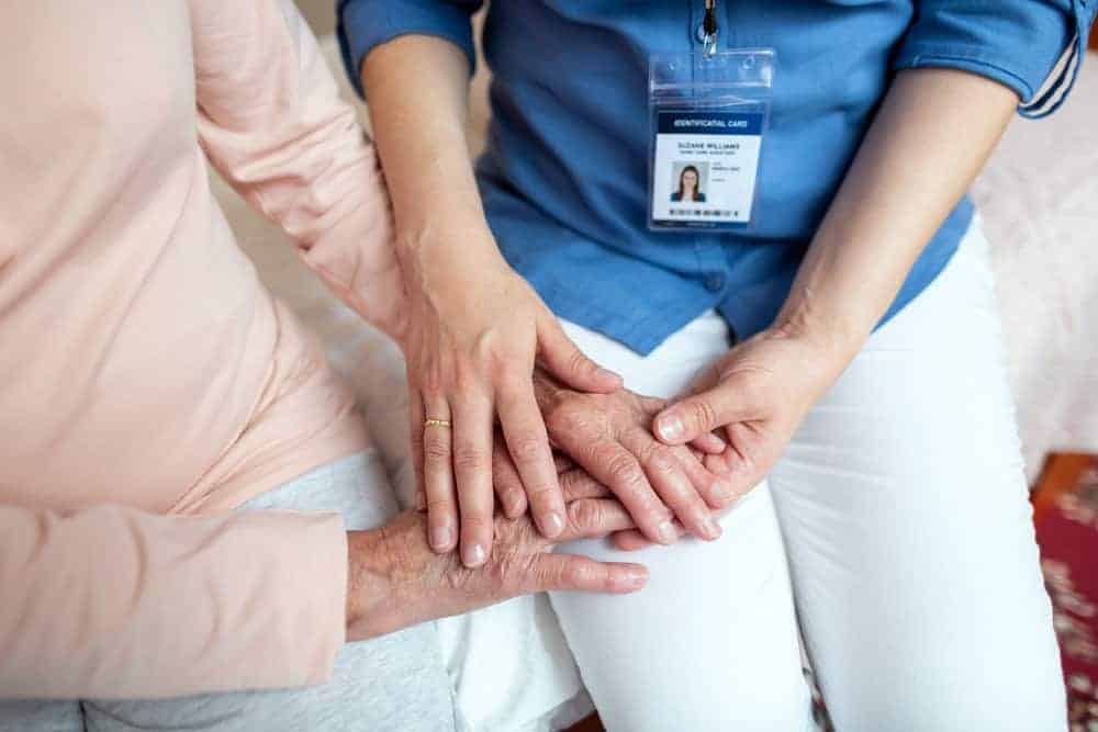 Close-up of a caregiver's hands providing comfort to a senior, symbolizing attentive caregiving.