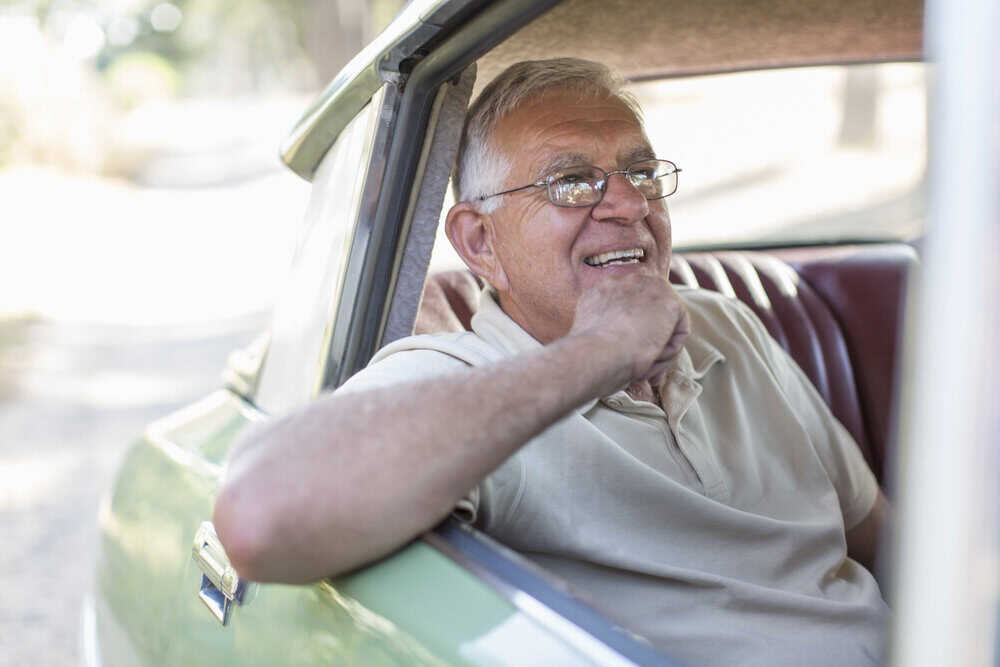 An elderly man looking thoughtful behind the wheel of a car, representing the decision to stop driving.